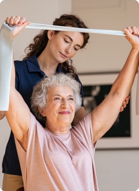 A younger woman assists an older woman with her exercise band.