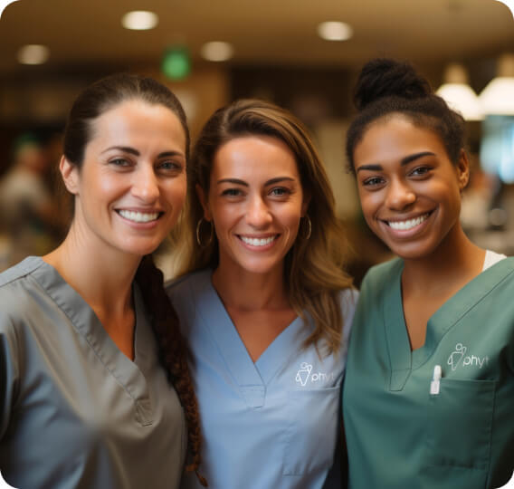 Three female healthcare workers in scrub suits smiling for the camera.