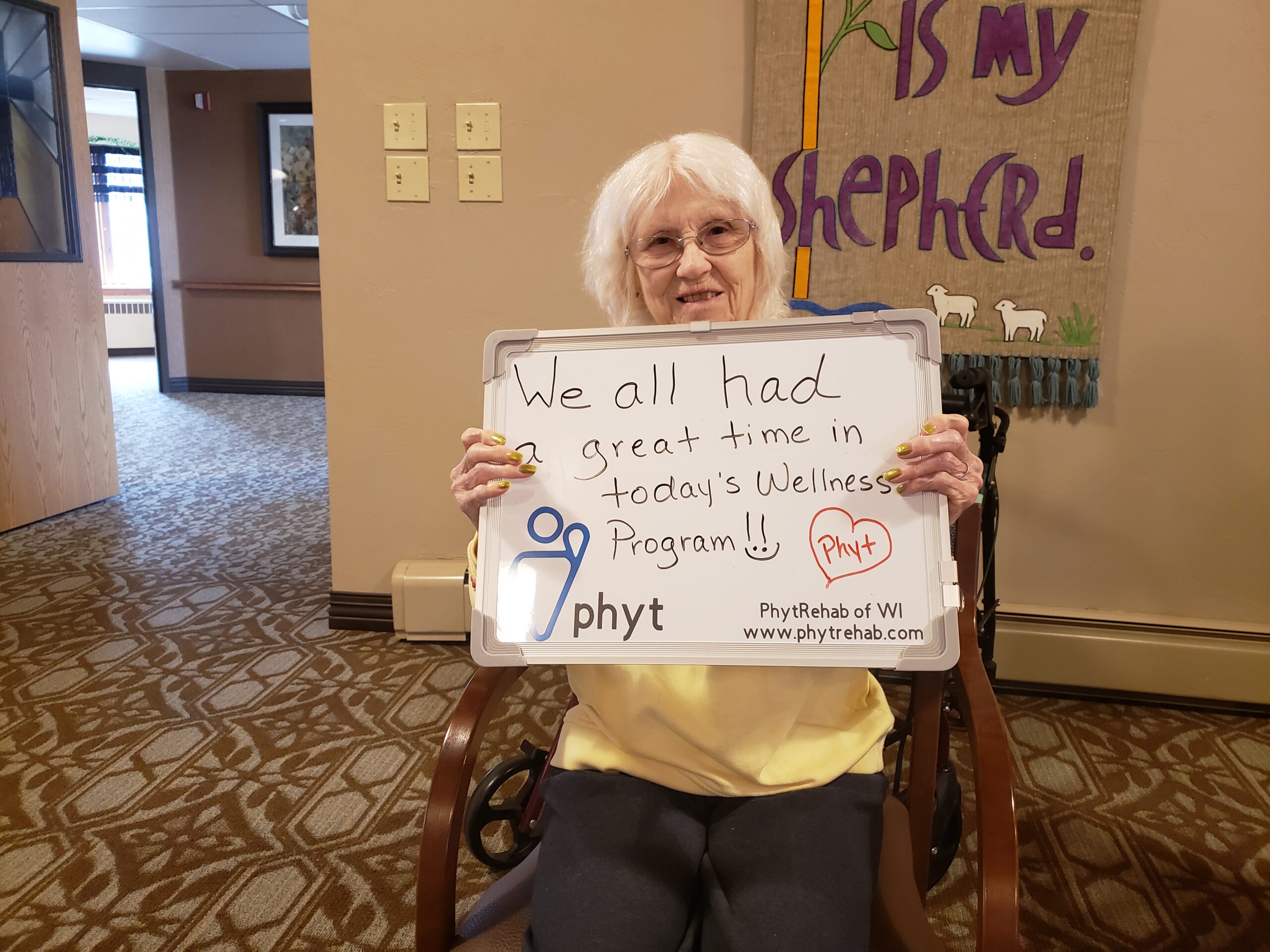 An older woman stands holding a sign that reads, "We all need to be fed," advocating for food security and support.