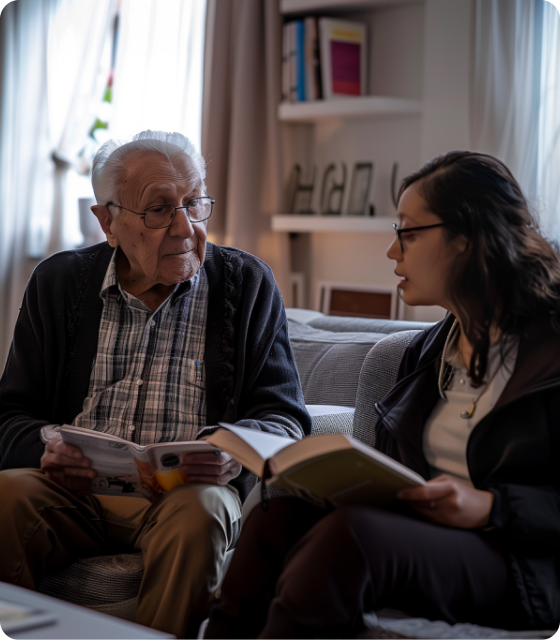 A woman and an older man sit together on a couch, both engaged in reading their respective books.